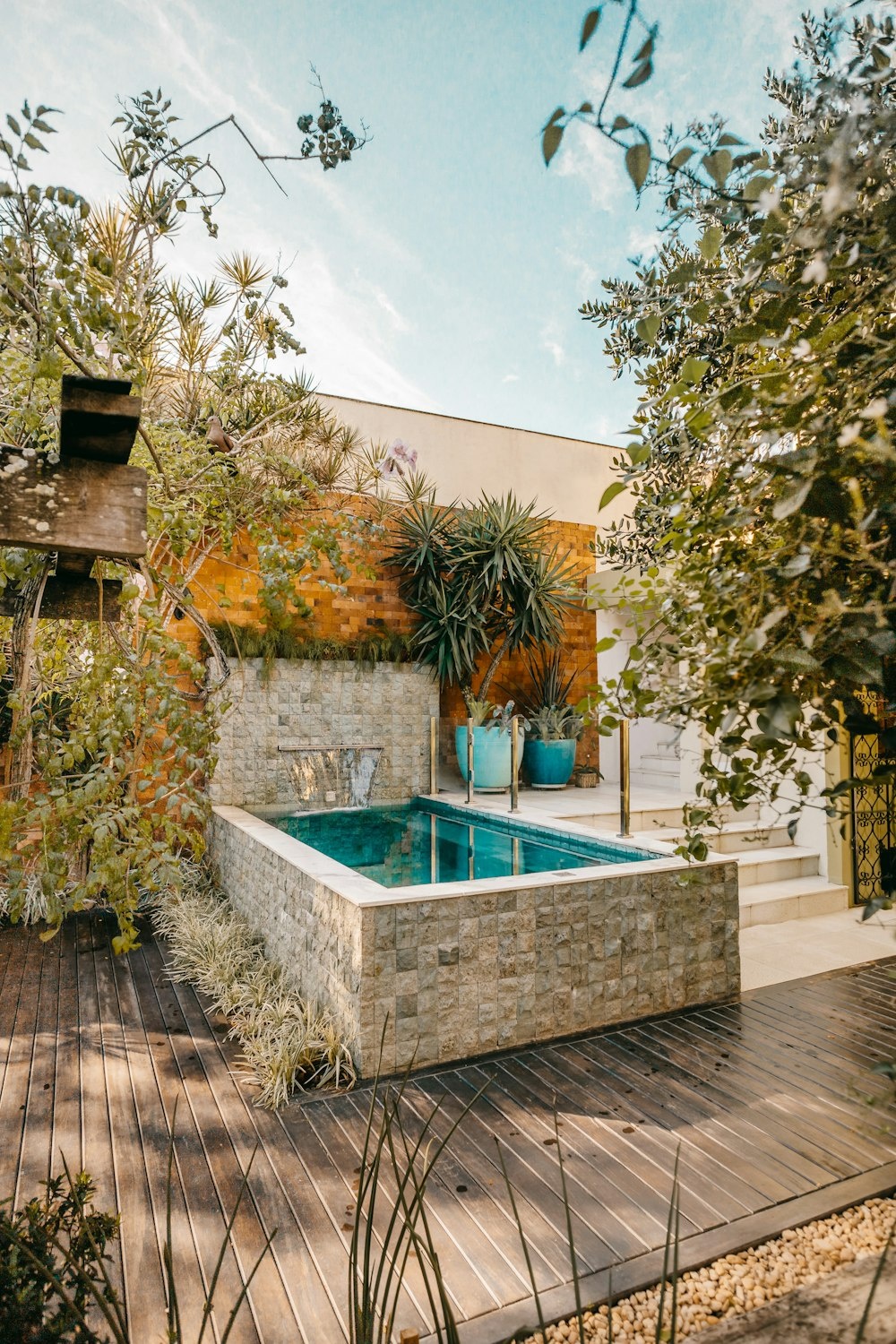 a pool with plants and a stone wall with a stone wall and trees
